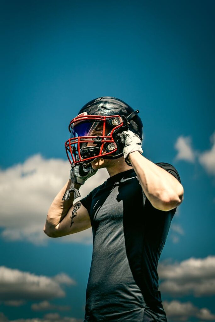 A football player in gear adjusting his helmet under a clear blue sky, ready for action.